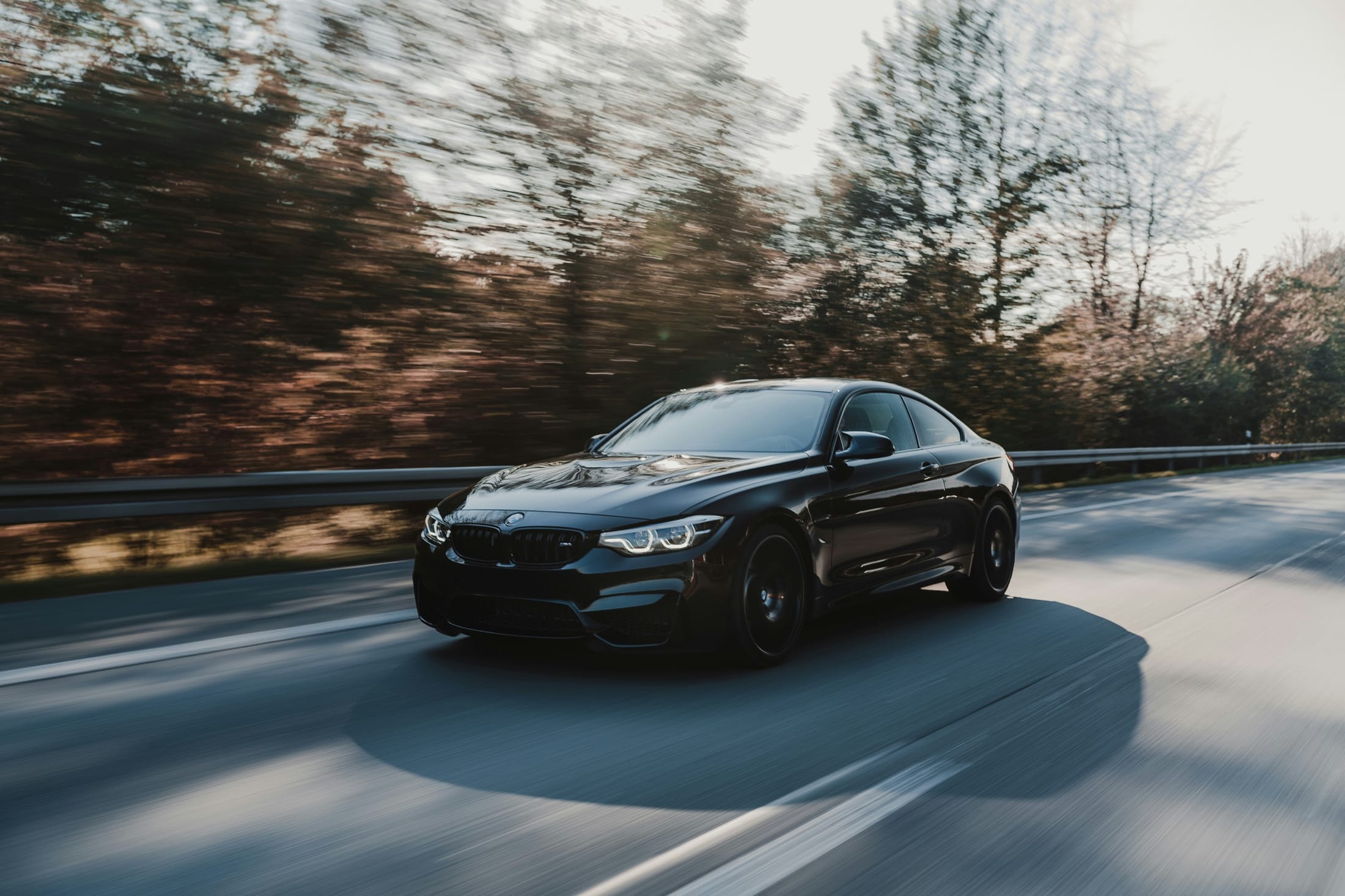BMW M4 noire en mouvement sur une route bordée d’arbres