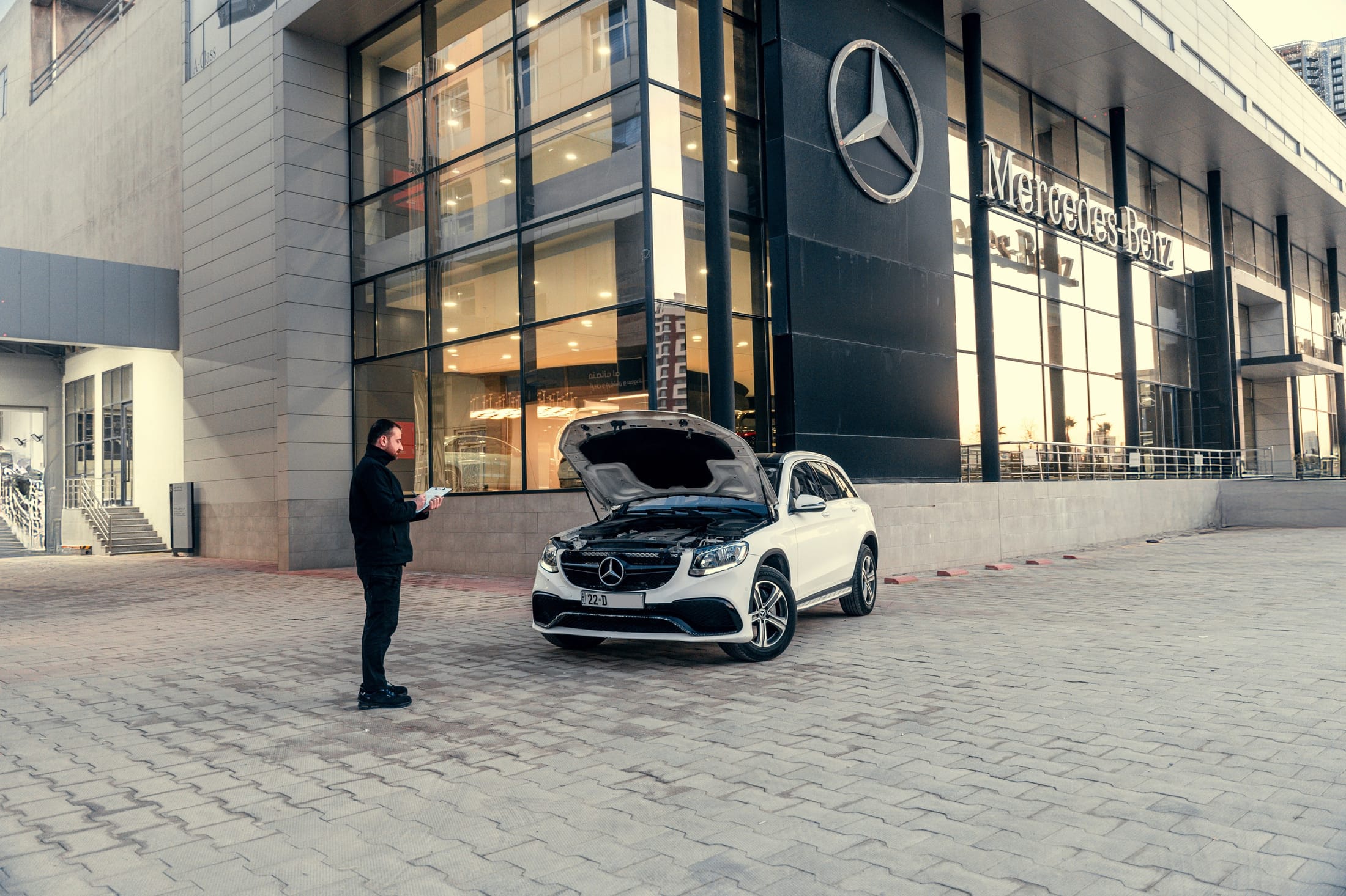 Inspection d’un SUV Mercedes capot ouvert devant une concession, carnet en main